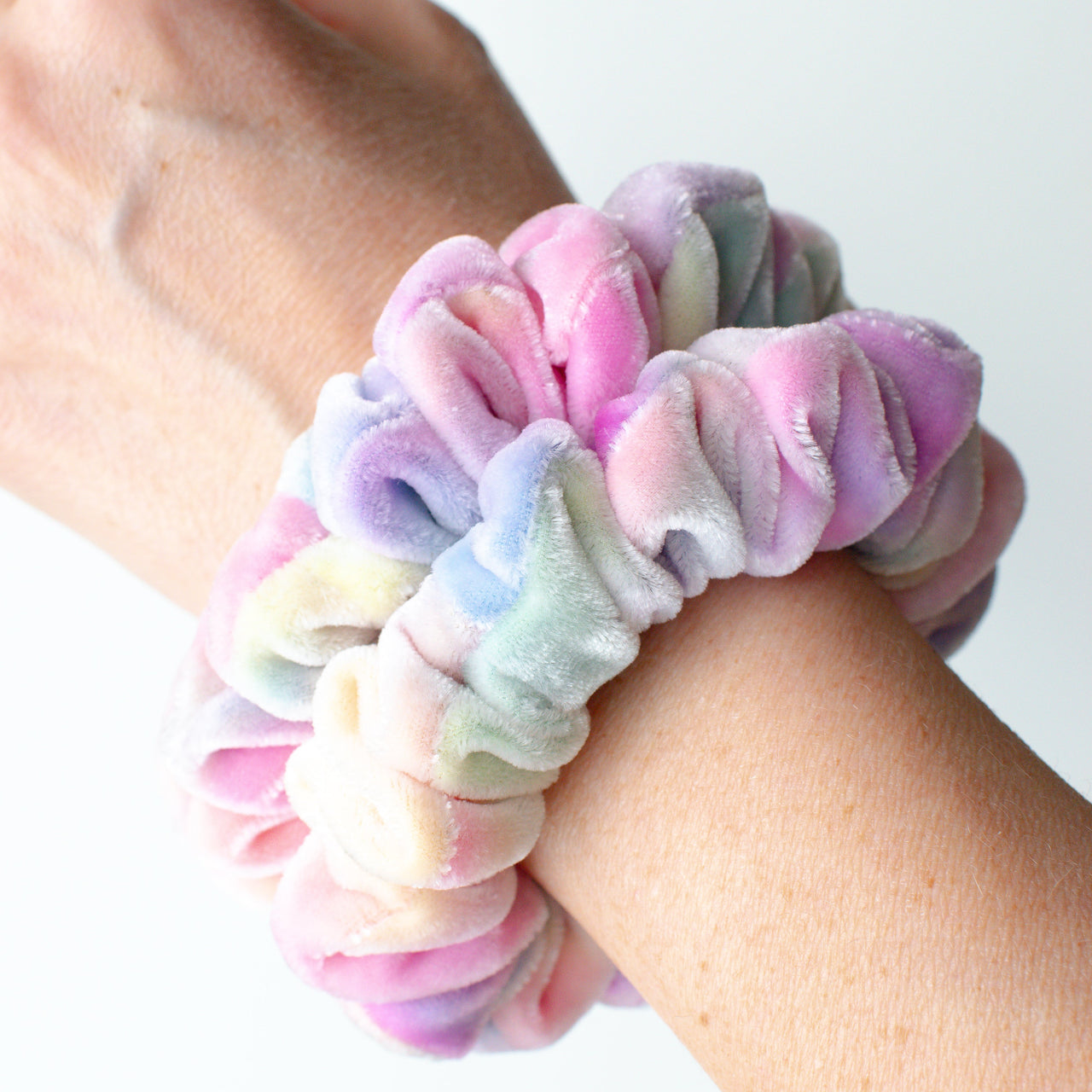 Pastel silk velvet scrunchie on a wrist against a white background