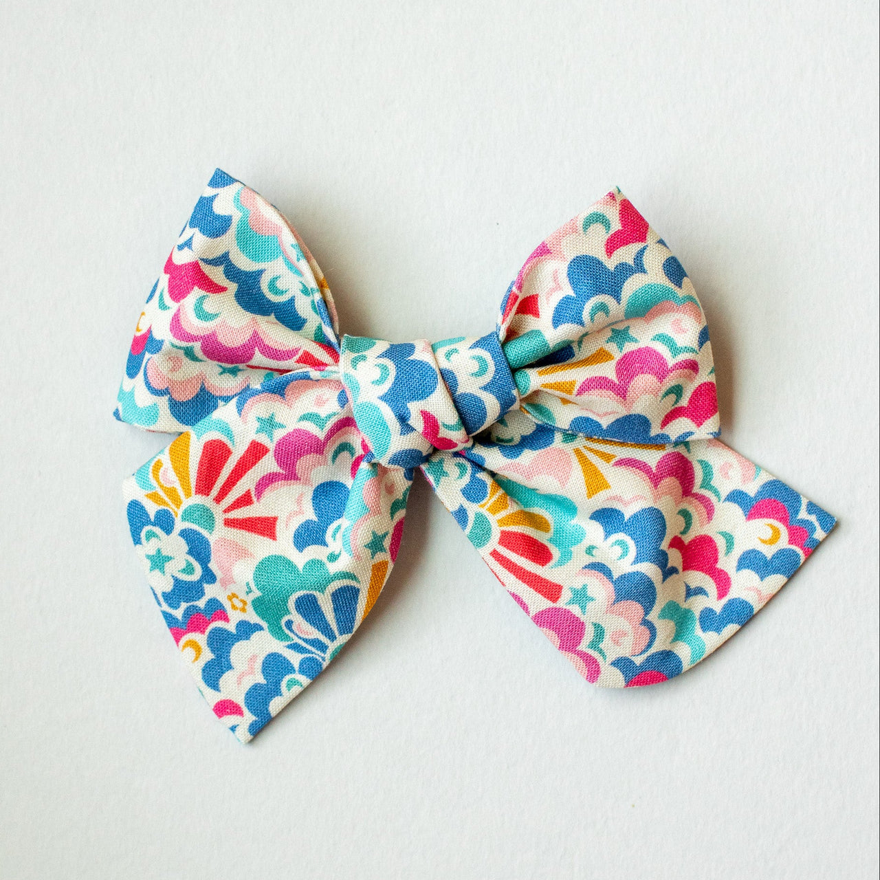 A multicolored fabric bow with a cloud and sunshine pattern, tied at the center and displayed against a neutral background.